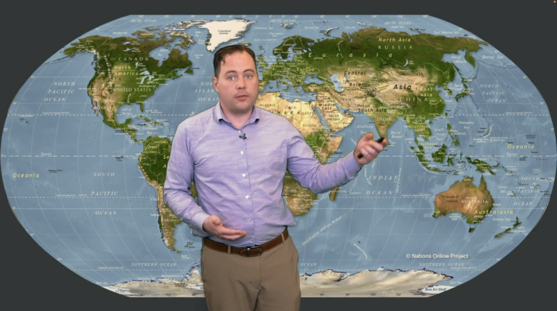 Screenshot of a presenter standing in front of a world map in a Full Screen Scene