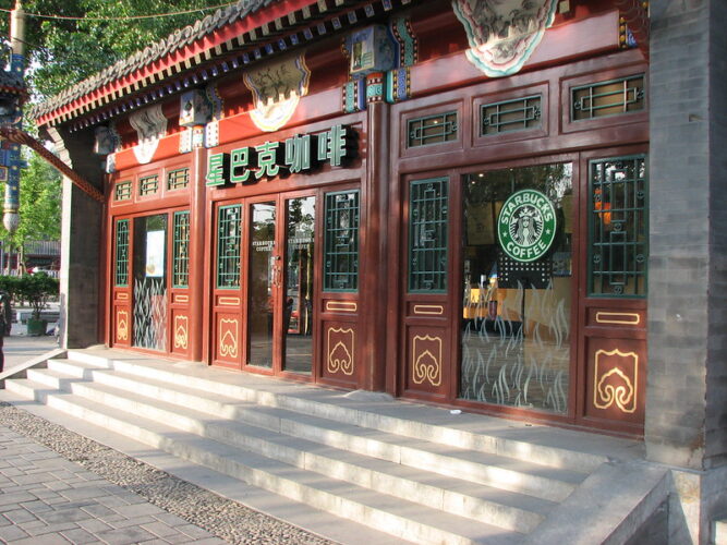 Traditional Chinese architectural style façade of a Starbucks coffee shop with red doors, wooden frames, and the iconic green logo on the window.