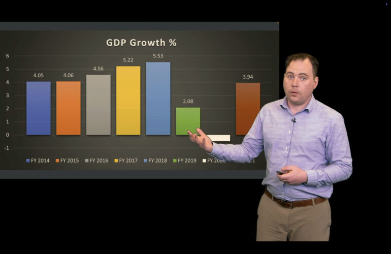 Presenter stands beside a bar chart