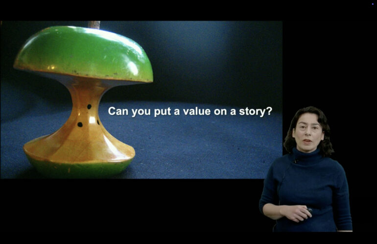 Video layout: presenter standing in lower right with a boxed slide at left, both against a black background.
